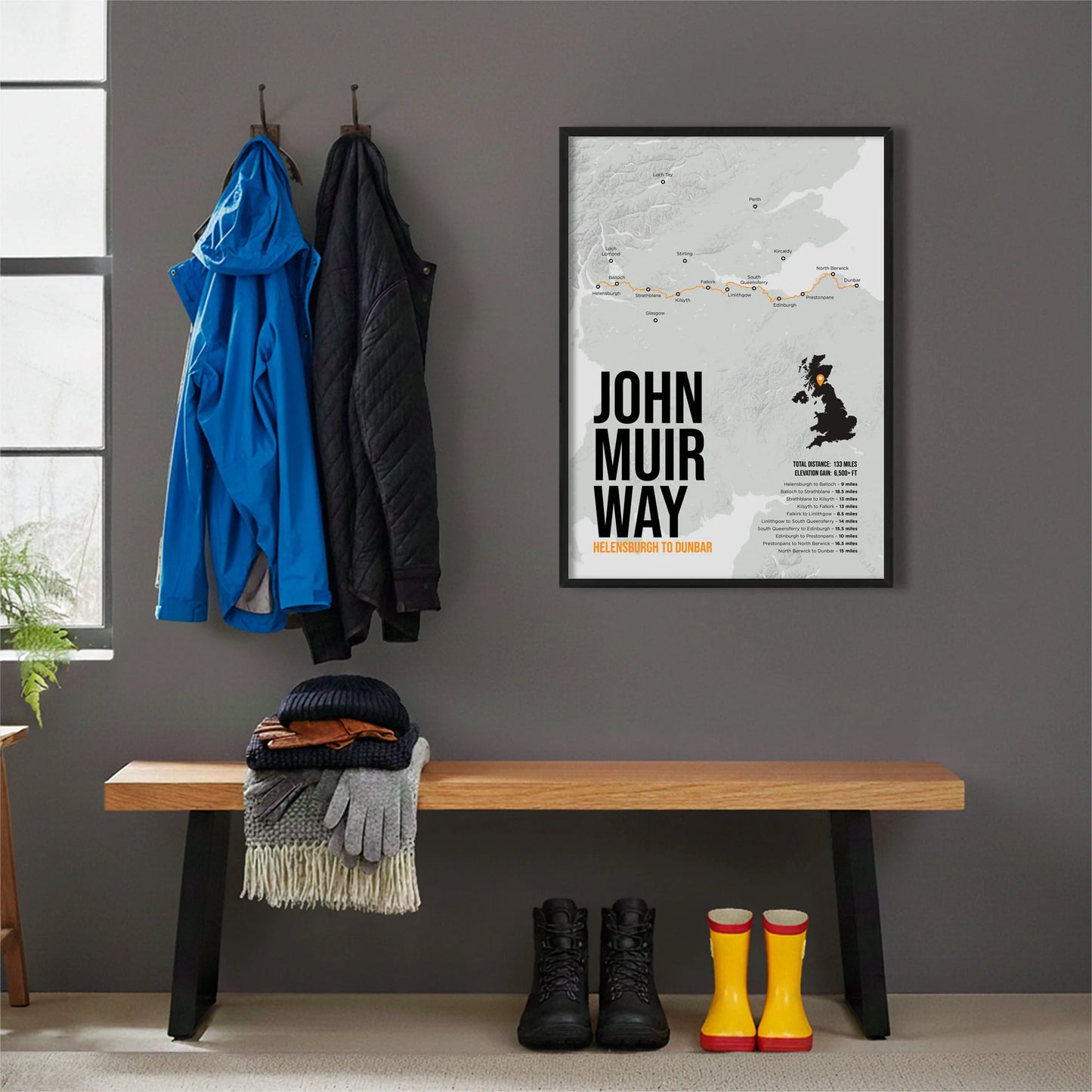 Framed print hanging on grey wall beside coats hanging above bench with walking boots and a scarf