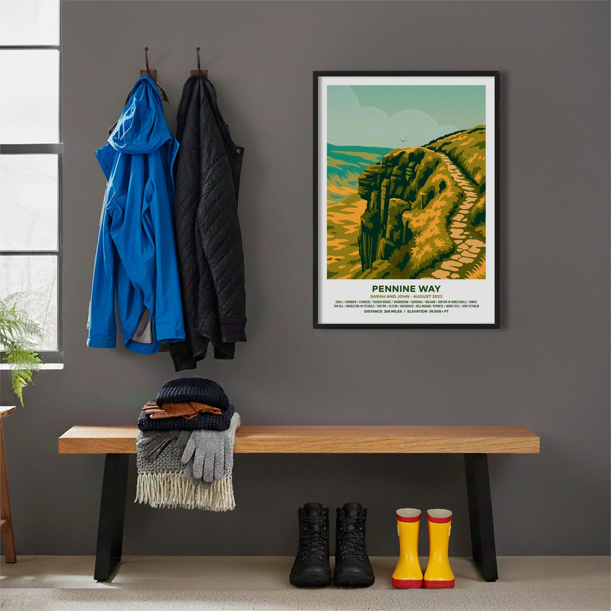 Framed print hanging on grey wall beside coats hanging above bench with walking boots and a scarf