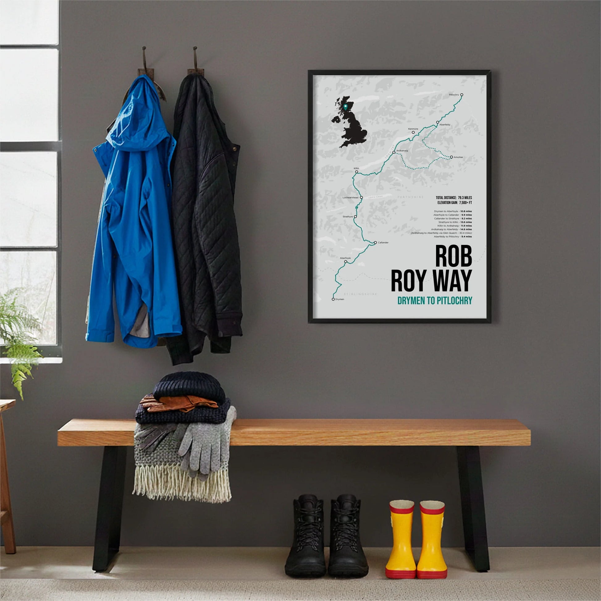 Framed print hanging on grey wall beside coats hanging above bench with walking boots and a scarf