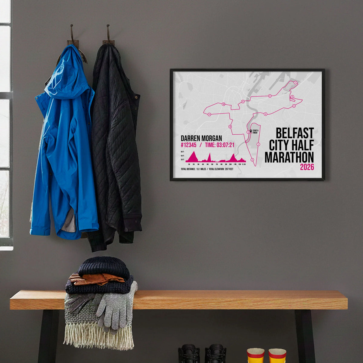Framed print hanging on grey wall beside coats on hooks above walking boots and shows