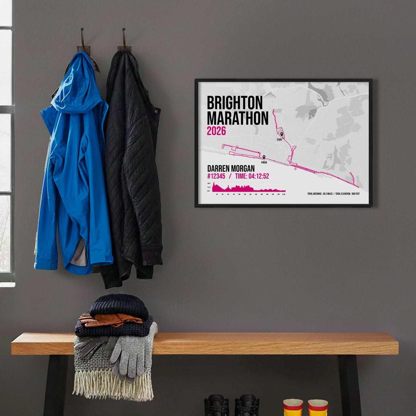 Framed print hanging on grey wall beside coats hanging above bench with walking boots and a scarf