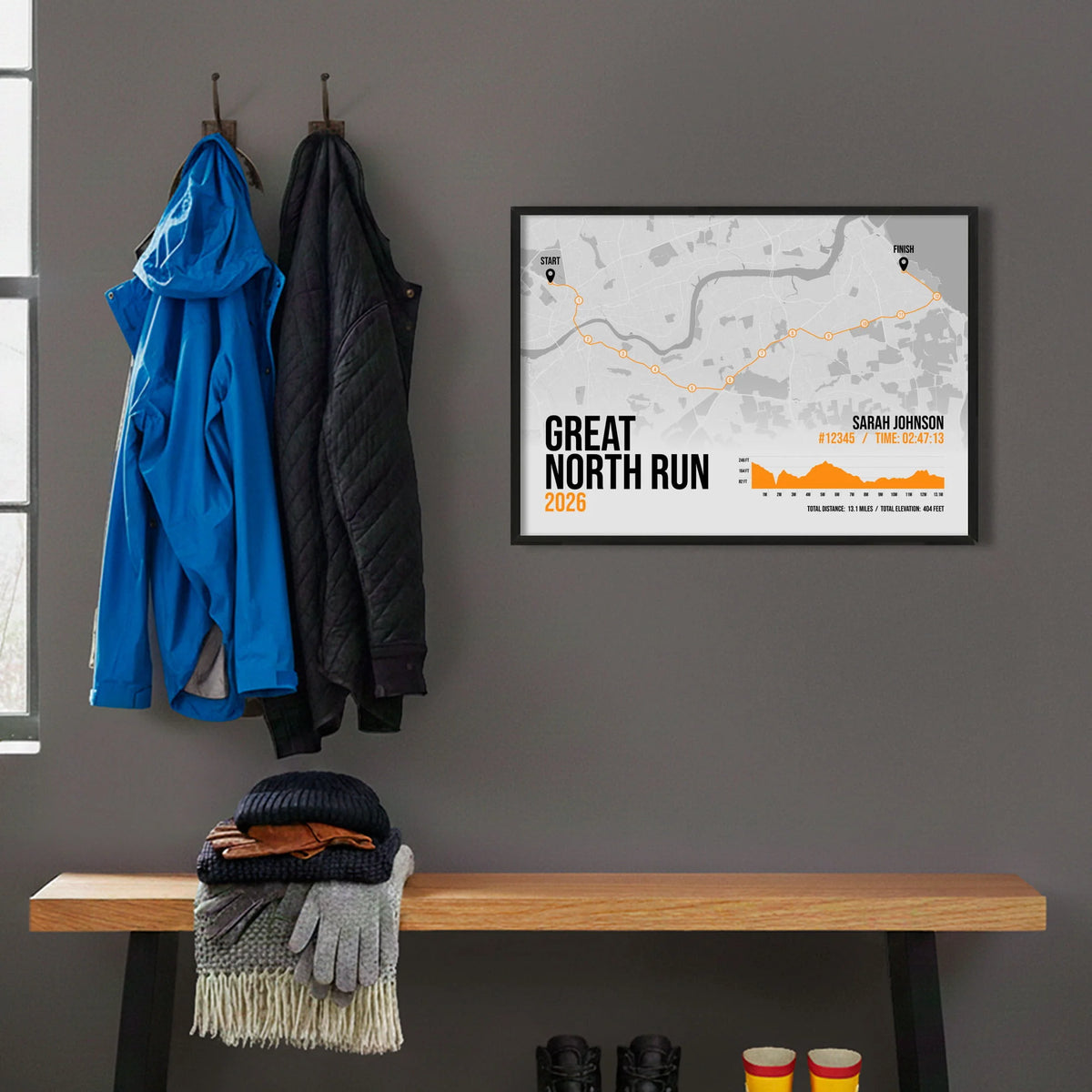 Framed print hanging on grey wall beside coats on hooks above walking boots and shows
