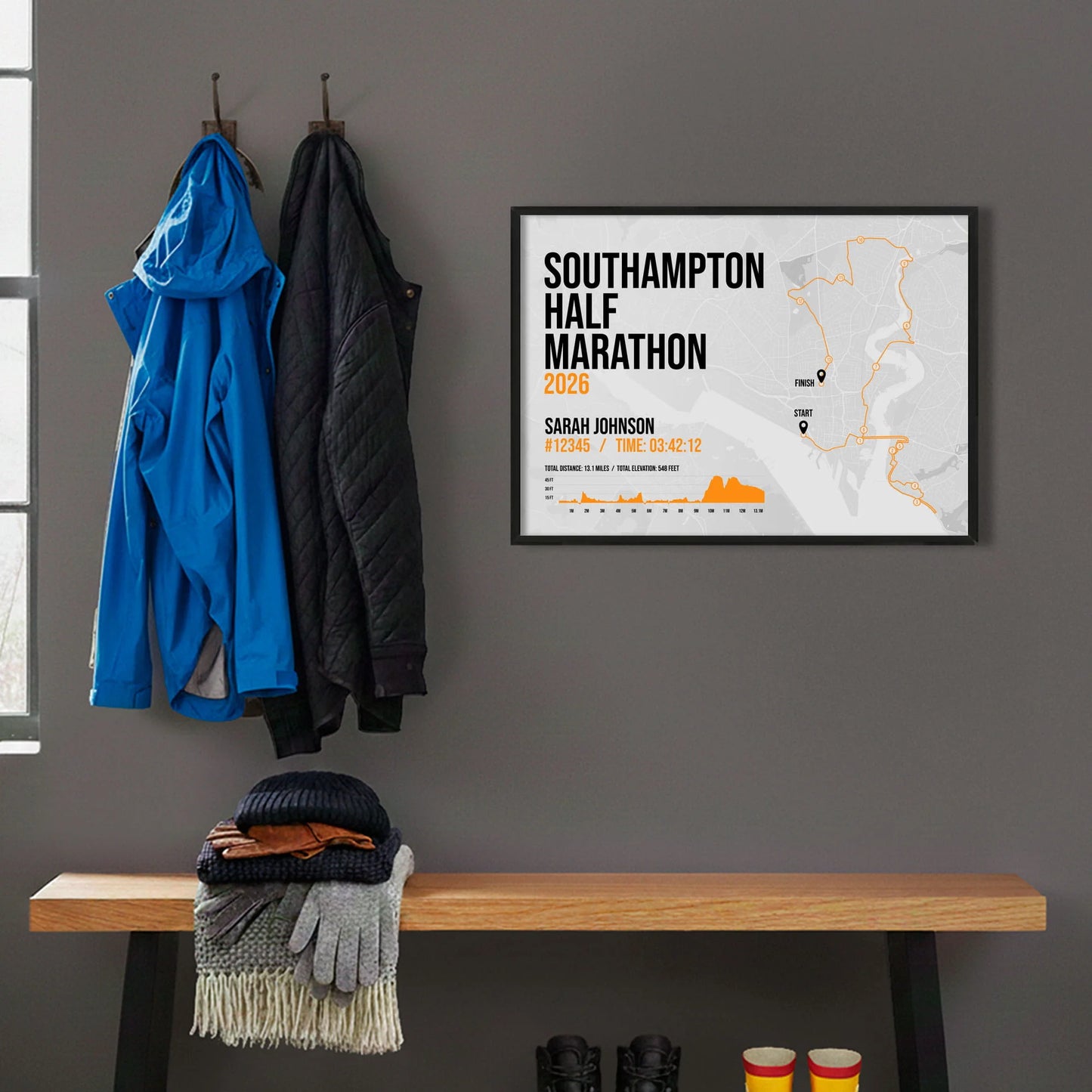 Framed print hanging on grey wall beside coats on hooks above walking boots and shows
