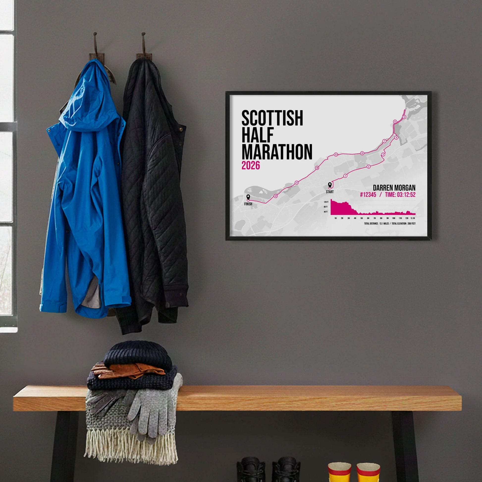 Framed print hanging on grey wall beside coats on hooks above walking boots and shows