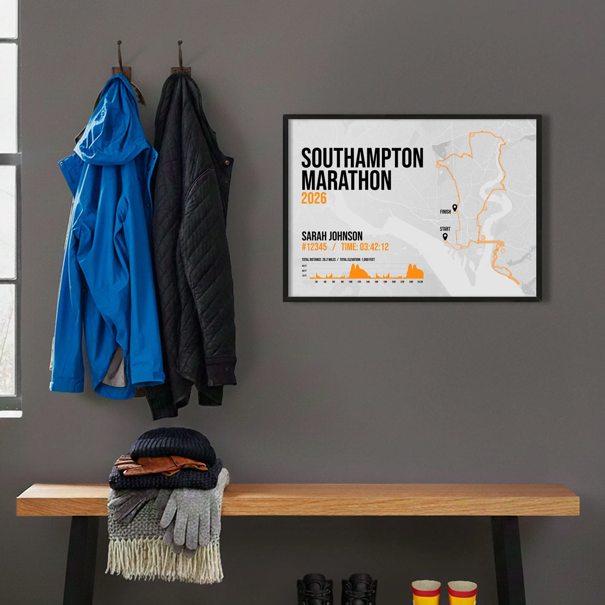 Framed print hanging on grey wall beside coats hanging above bench with walking boots and a scarf