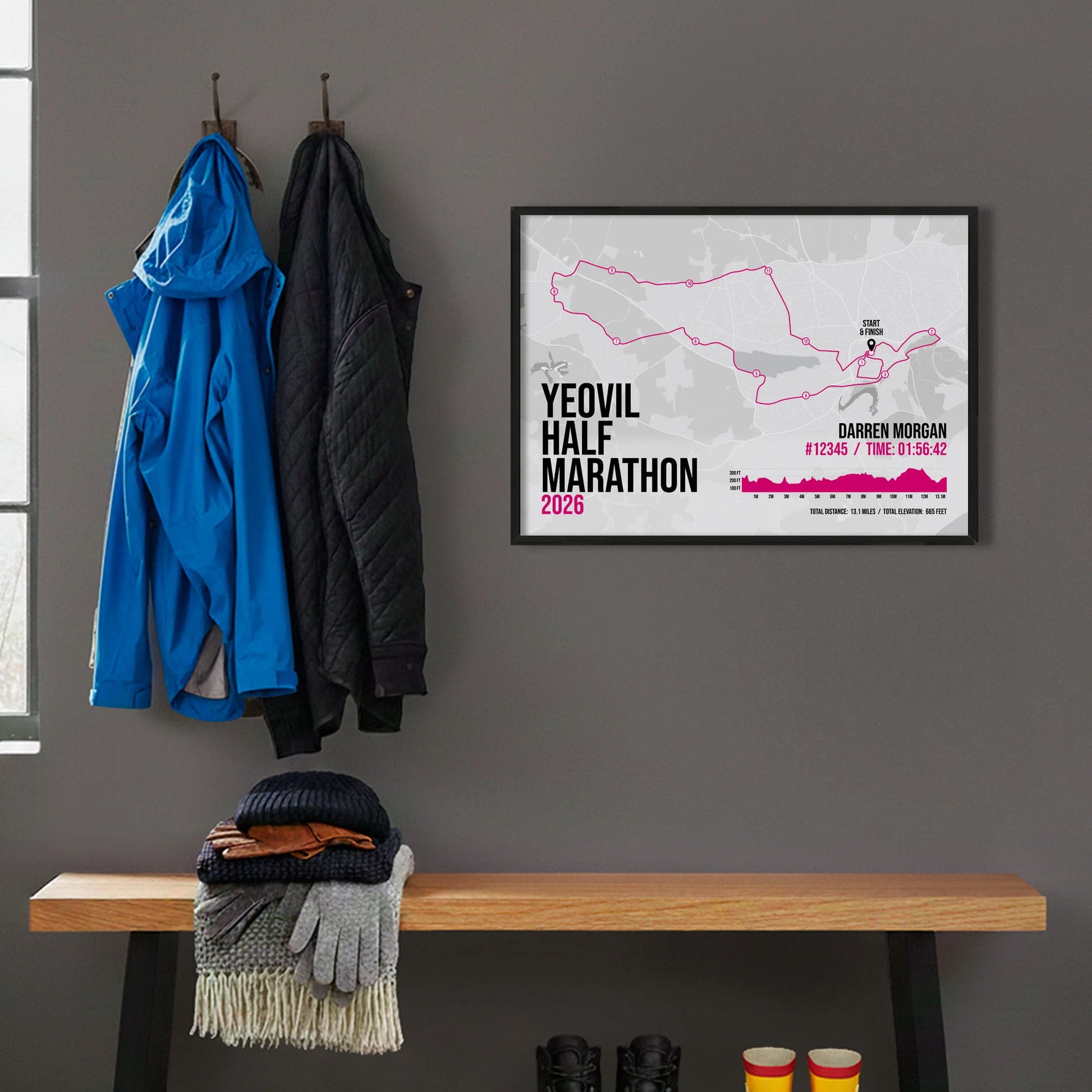 Framed print hanging on grey wall beside coats hanging above bench with walking boots and a scarf
