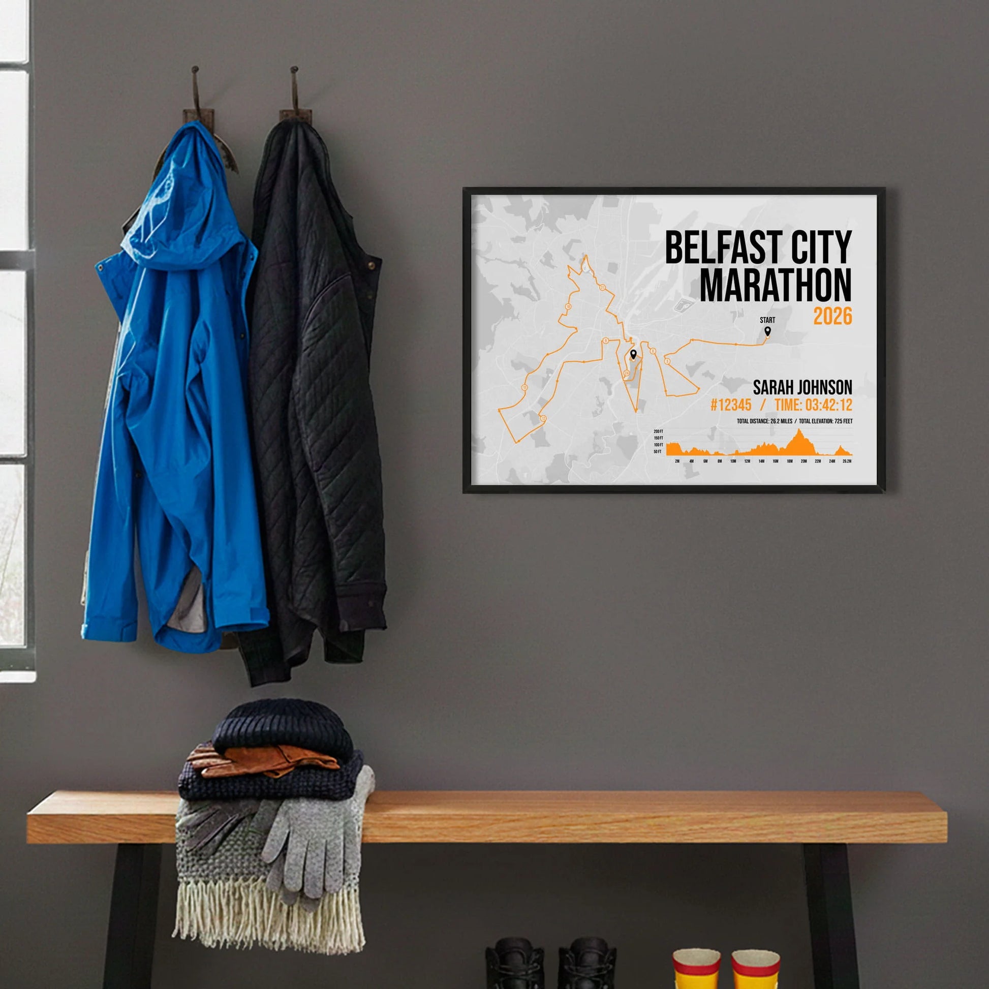 Framed print hanging on grey wall beside coats hanging above bench with walking boots and a scarf