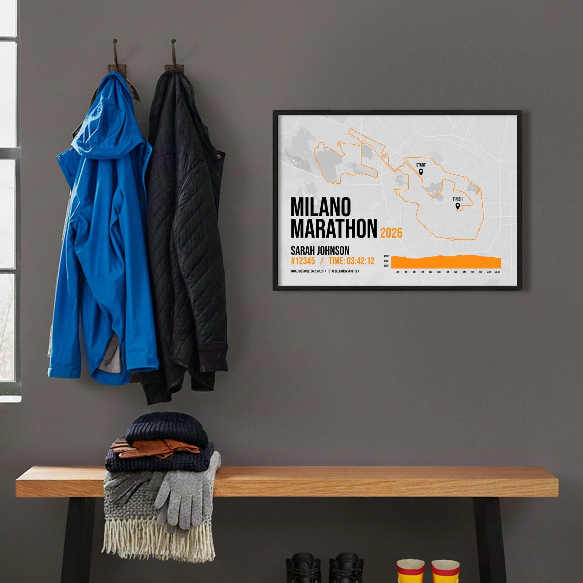 Framed print hanging on grey wall beside coats hanging above bench with walking boots and a scarf