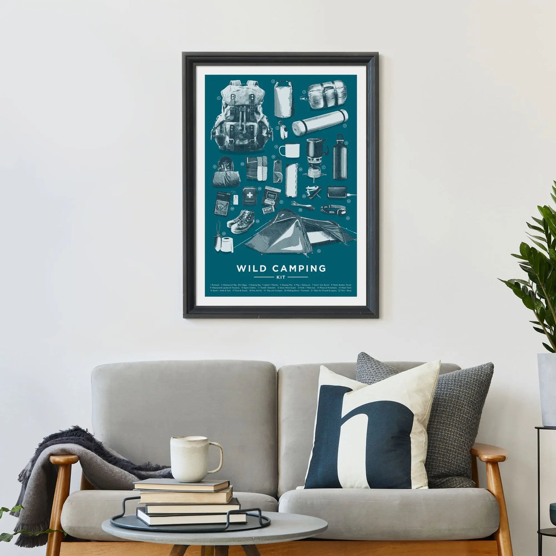 Large print on wall behind a 2 seater sofa covered in cushions with a coffee table covered in books.