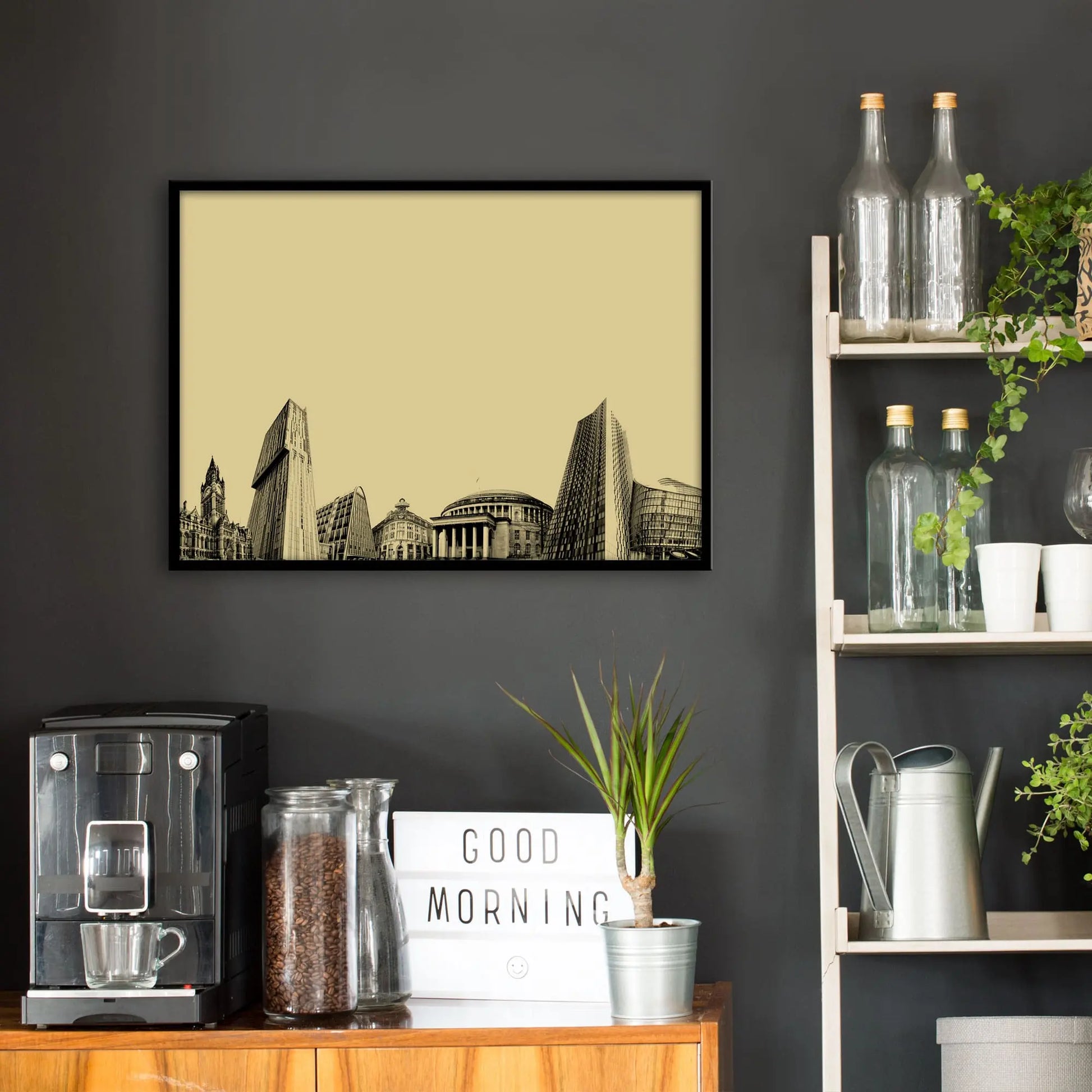 Kitchen wall infront of which is a sideboard with a coffee machine and a set of shelves holding bottles and plants. On the wall above the sideboard is the framed print in a black frame on a dark grey wall.