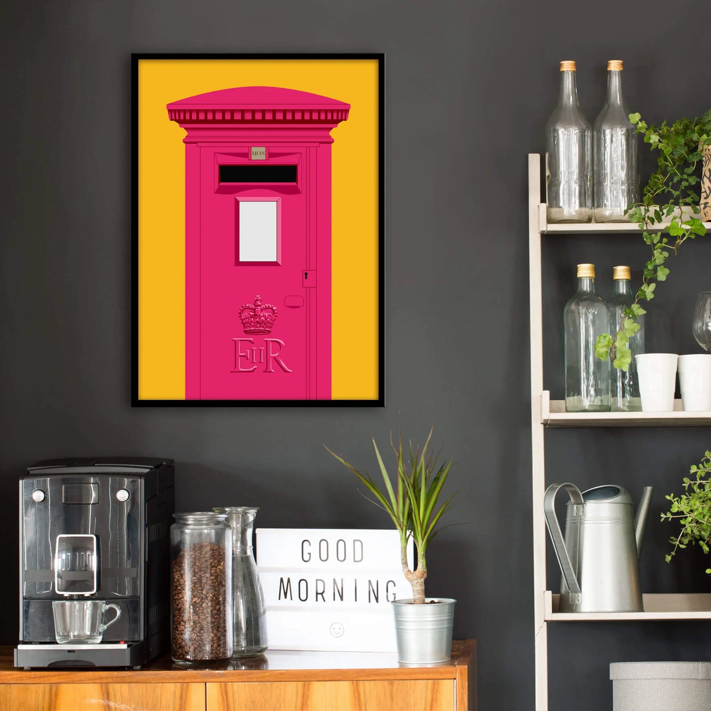 Kitchen wall infront of which is a sideboard with a coffee machine and a set of shelves holding bottles and plants. On the wall above the sideboard is the framed print in a black frame on a dark grey wall.